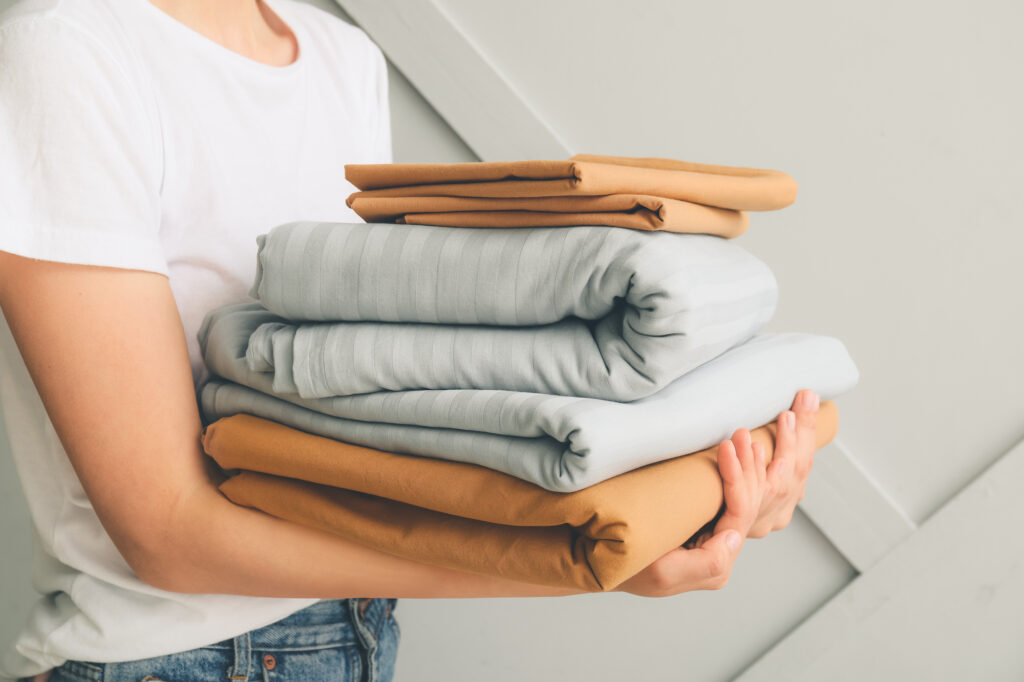 Best Material for Bed Sheets Woman with a stack of bedsheets