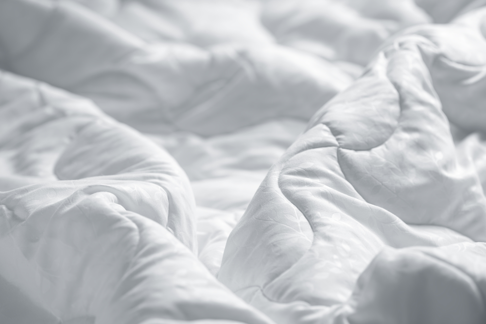 Quilt vs. Comforter vs. Duvet A white blanket is wrinkled on a bed