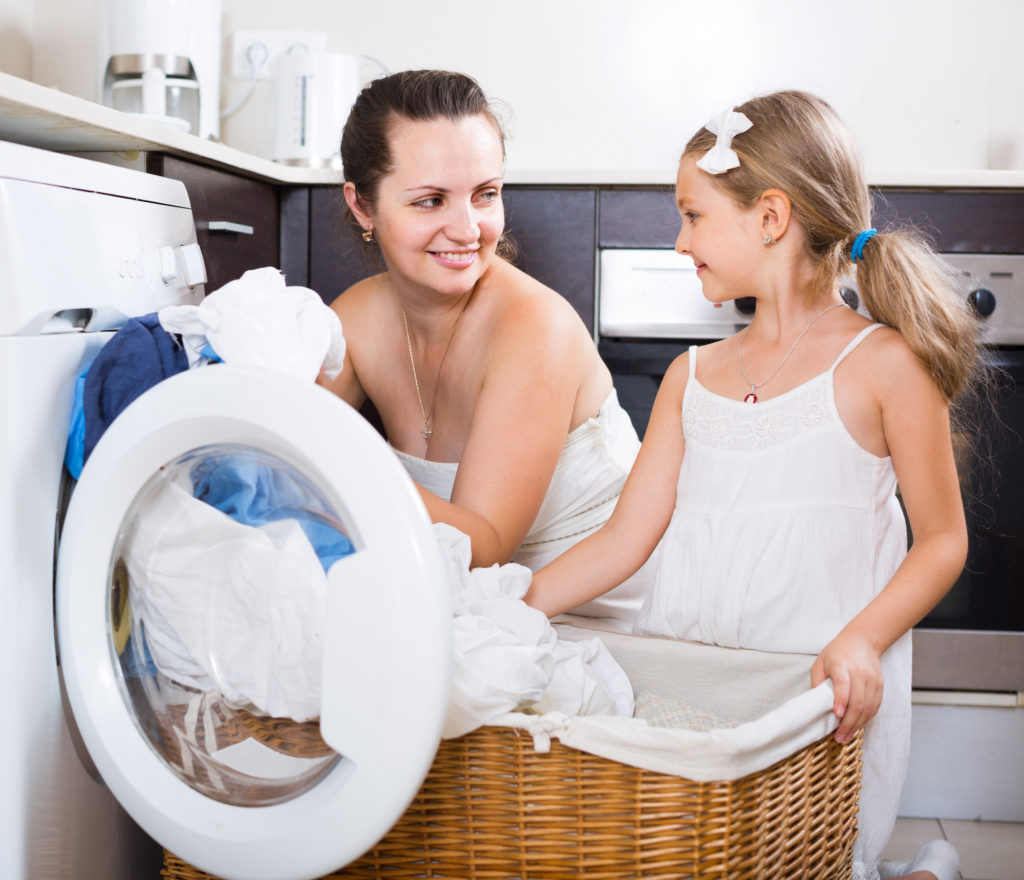 How to Wash Your Sheets woman and child washing sheets with a washing machine